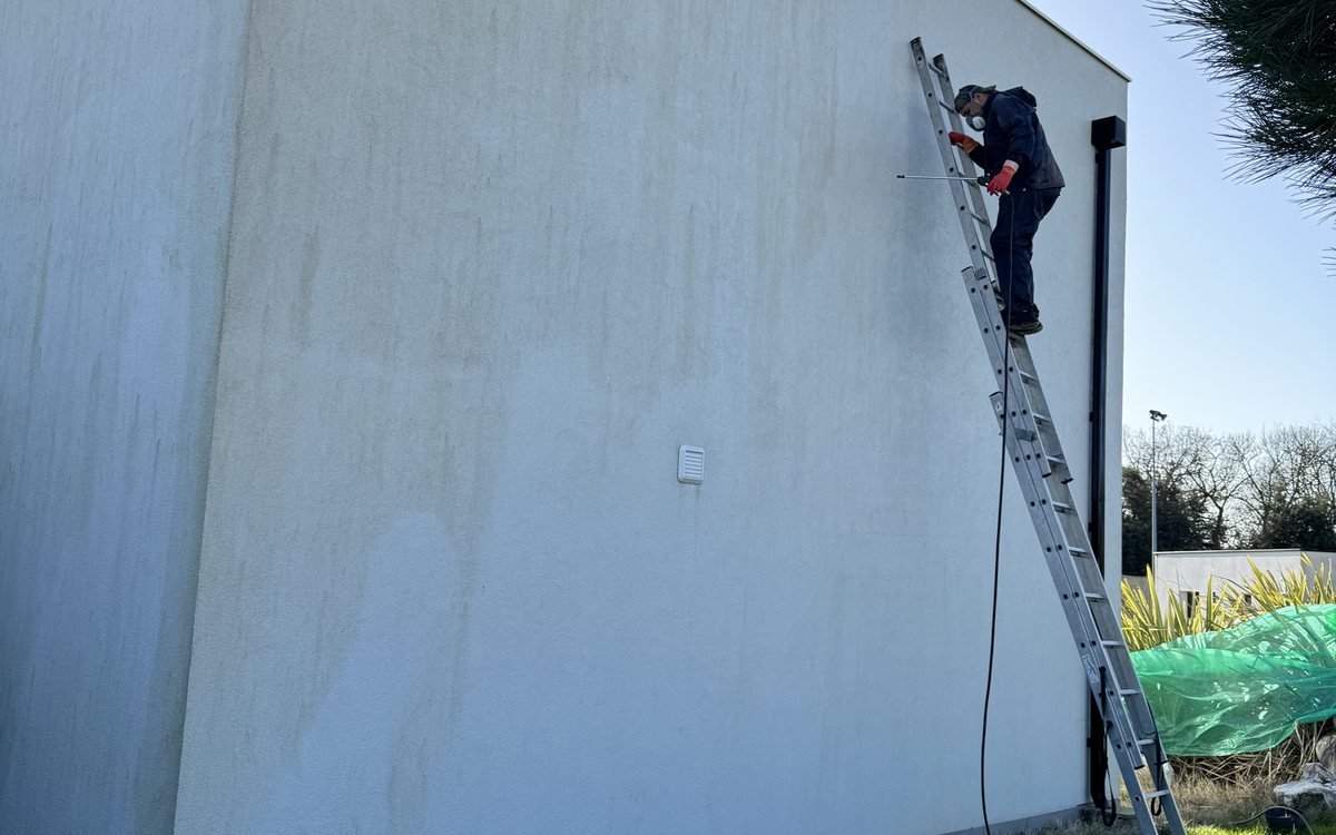 Application d’un traitement de nettoyage sur une façade encrassée depuis une échelle, chantier à Préserville