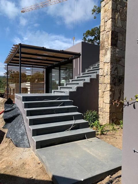 Escalier extérieur en pierre grise desservant une terrasse sous pergola
