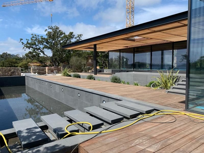 Terrasse en bois exotique et bassin bordé de pierre grise devant une villa contemporaine