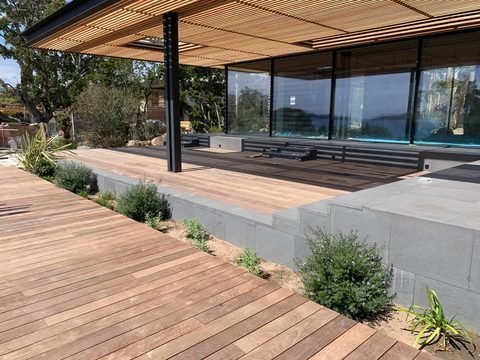Large terrasse en bois exotique bordée d’un muret en pierre et de plantations