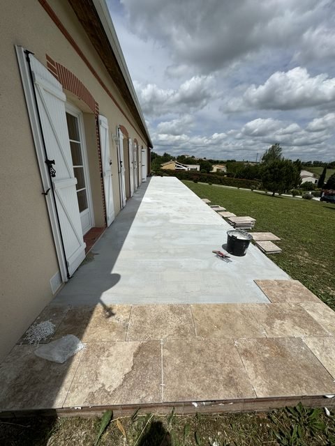 Terrasse en travertin en cours de pose le long d’une maison à Bannières